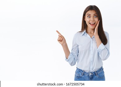 Girl screaming from surprise and happy emotions as found something awesome in store, telling about cool exciting event, pointing finger left, staring camera impressed, stand white background