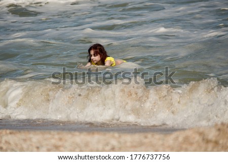 Girl at sea. The portrait of the young girl. Teenager summer vacation sand. Sunny day and the sea. Childhood travel vacation. Teenager in a yellow swimsuit on the beach. Teenager swims in the sea