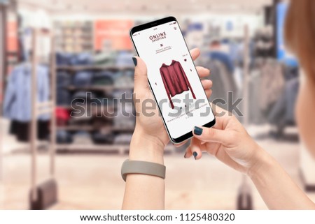 Girl searching for clothes with smartphone, clothing store in background