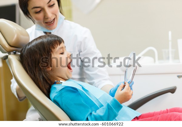 Girl seating in dental office and looking at her\
teeth the mirror