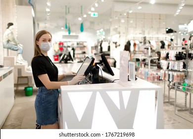 Girl seller in a mask and gloves stands at the checkout in a store. Store seller during COVID-19. Safety during the virus. The seller in the clothing store.