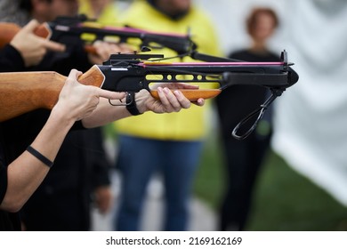 Girl Shoots From A Crossbow Close-up. A Young Girl Is Aiming At A Target With A Crossbow. Girl Shoots From A Crossbow In A Summer Outdoor Shooting Range.