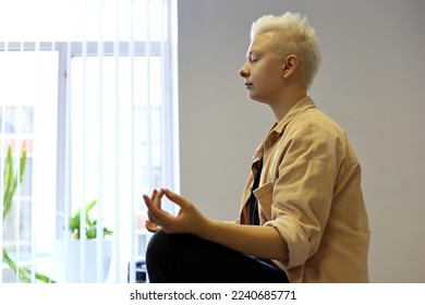 Girl with short blonde hair sitting in lotus position. Practicing yoga, meditation at work - Powered by Shutterstock