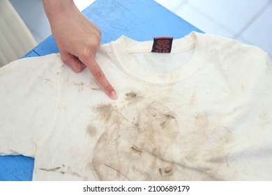 Girl Showing Dirty Stain On Kid Shirt With Finger Pointing  From Playing Hard On Mud Stain. Dirty Stain For Cleaning Concept Work.