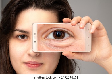 Girl showing the magnified photo of eye bag through her smart ph
