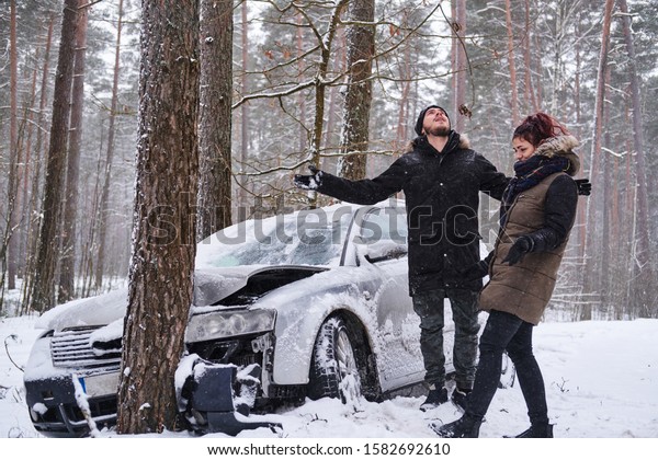 Girl shows her boyfriend the damage to his\
car after the accident. The girl crashed her boyfriend\'s car.\
Crashed car after accident in snowy\
forest