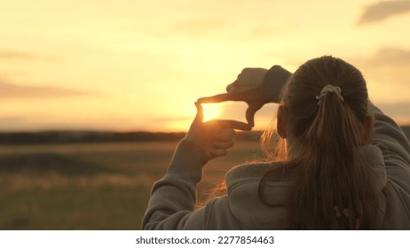 Girl shows her fingers frame symbol, sun. Hands of young female director cameraman making frame gesture at sunset in park. Sees like in movies. Concept of seeing world as different. Business planning