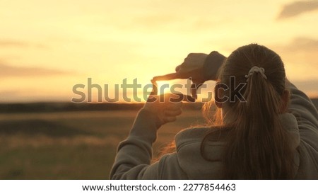 Girl shows her fingers frame symbol, sun. Hands of young female director cameraman making frame gesture at sunset in park. Sees like in movies. Concept of seeing world as different. Business planning