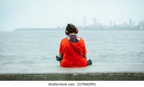 A Girl Siiting With Her Back On The Seaface Listening To Music With Matching Headphones And Top