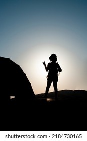 Girl Silhouette On A Bridge Holding Up Two Fingers As A Victory Sign, Against Bright Evening Sun.