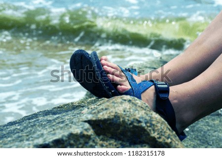 A girl is siting on the rock at the beach and that is her feet.                