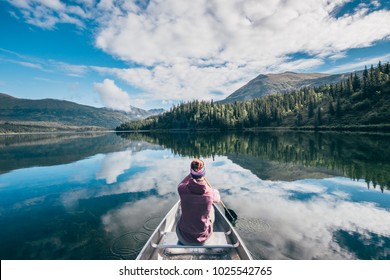 A girl sits in a canoe in a mirroring lake during in Alaska - Powered by Shutterstock