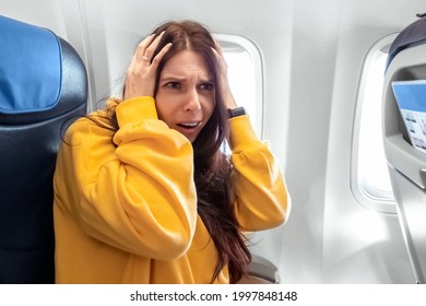 A Girl Sits In Front Of An Airplane Window And Is Nervous, Afraid To Fly, The Cabin Of A Passenger Airliner. Aerophobia, Phobia, International Flights, Stress, Motion Sickness