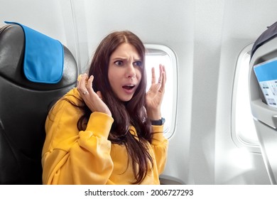 A Girl Sits In Front Of An Airplane Window And Is Nervous, Afraid To Fly, The Cabin Of A Passenger Airliner. Aerophobia, Phobia, International Flights, Stress, Motion Sickness