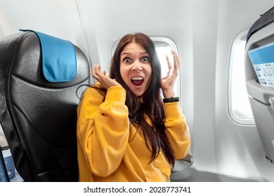 A Girl Sits In Front Of An Airplane Window And Is Nervous, Afraid To Fly, The Cabin Of A Passenger Airliner. Aerophobia, Phobia, International Flights, Stress, Motion Sickness