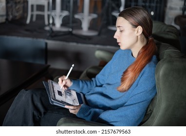 A Girl Sits In The Lobby Of A Hotel Or Restaurant And Works On Apartment Design On Electronic Tablet. The Concept Of Inspiration, Creativity, Self-development, Hobby, Modern Art. Remote Work. Modern T