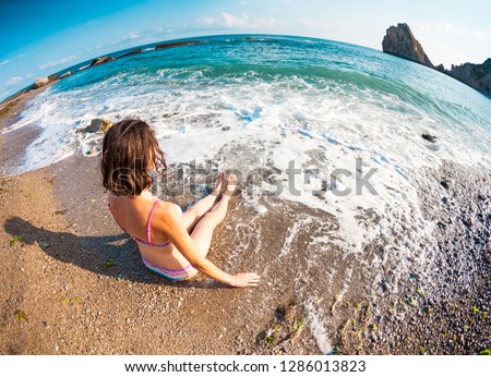 The girl sits on the beach. Woman bathes in the ocean. Rest on the coast. Slender brunette in a swimsuit sitting on the beach.