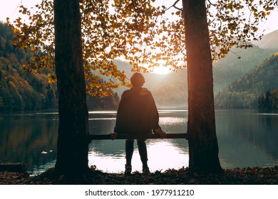 A girl sits on a bench and looks at Lake Ritsa at sunset in Abkhazia. Mountain landscape