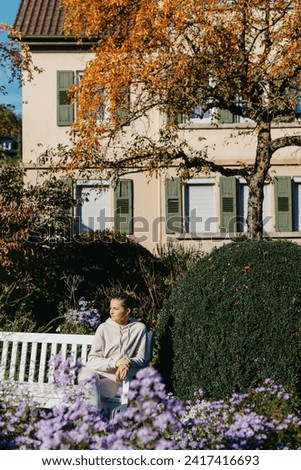 A Girl Sits On A Bench In The Park And Enjoys The Sun. Portrait Young Adult Attractive Woman Enjoy Sitting On Bench And Relaxing Calm Carefree Rest In City Park Against Green Grass And Trees On Sunny