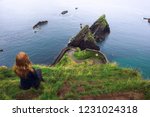 Girl sits on a cliff over the ocean and the Dunquin Pier situated on the west coast of the Dingle Peninsula in Ireland