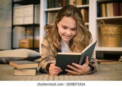 girl sits on the couch and reads a book, a tablet and headphones lie next to it. modern teenager at home. teen literature concept.