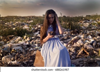 A Girl Sits On A Dump With Old Suitcase And An Empty Purse