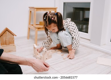 Girl Sits On The Floor In A Room And Plays With Her Dad In A Natral Wood Constructor. Wooden Childrens Construction Kit. Toys Made Of Eco-friendly Material. The Castle Is Made Of Wooden Cubes.