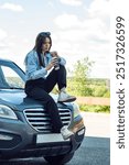 A girl sits on the hood of a car and drinks coffee.