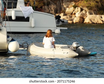 The Girl Sits On An Inflatable Dinghy Boat Moored To The Stern Of A Sailing Yacht. Communication Of The Yacht With The Shore. Charter Fleet Team. Work On The Ship. Navigation Safety. Rest After A Day