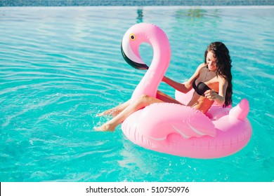 girl sits on inflatable mattress flamingos in the pool