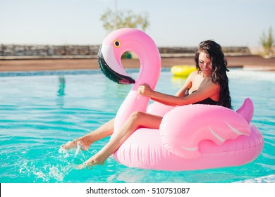 girl sits on inflatable mattress flamingos in the pool