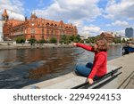 A girl sits on a parapet on the banks of the Brda River in Bydgoszcz. People visit riverfront in Bydgoszcz. Bydgoszcz is the capital of region Kujawsko-Pomorskie visited by 2.25m tourists annually 