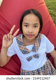 The Girl Sits On The Red Sofa And She Is Holding Up Two Fingers.