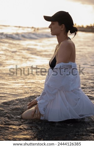 A girl sits on the seashore at dawn, personifying calm and serenity. Popularizes tourism, resorts, healthy lifestyles and outdoor sports.