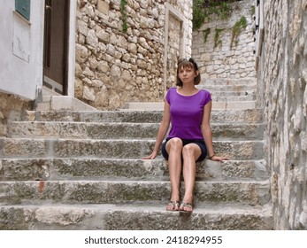 A girl sits on the stairs on the street in the city of Rovinj (Croatia).                    