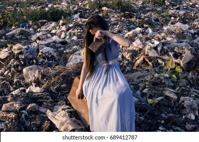 The Girl Sits On A Suitcase With An Empty Purse Among The Garbage Dump And Cries