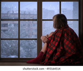 Girl Sits On The Window Sill Of The Window And Looks At The Falling Snow. The Concept Of Home Comfort, Season, Solitude