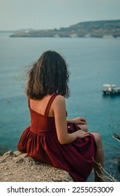 
A girl sits over a cliff.Woman on a rock.Resting on the sea.Mediterranean sea.Travel agency.Lady in red.Portrait of a girl at sunrise.Sea tourism and vacation.Woman looks at the sea.Calmness.Pleasure - Shutterstock ID 2255053009