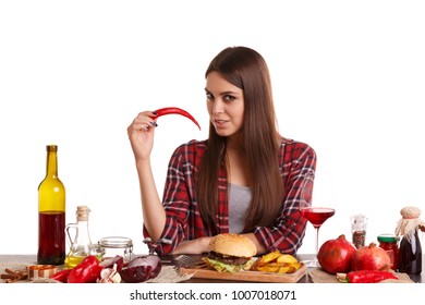 A girl, sits at a table with food and is holding a chili pepper. Isolated on white background.