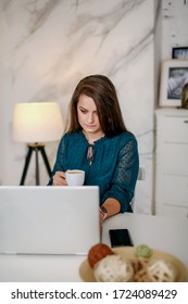 A Girl Sits At A Table In The Office Filling A Contract Or Financial Report With A Cup Of Coffee. Types On A Laptop. There Are Documents On The Table. Image With Selective Focus