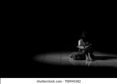 A girl sitting alone with a doll in a dark room.