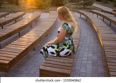 The Girl Is Sitting Alone In Her Back Among The Many Benches Of The Street Theater