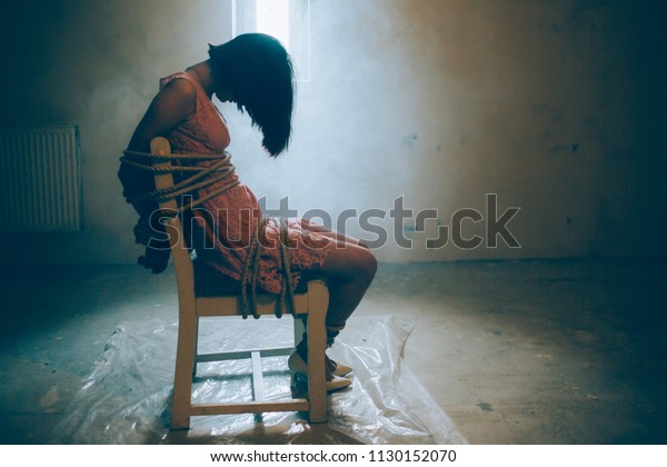 女の子は一人で座っている 彼女の手足はロープで椅子に縛り付けられている 女の子は下を向いている 彼女は意識を失った 彼女は小さな窓の前に座っている の写真素材 今すぐ編集