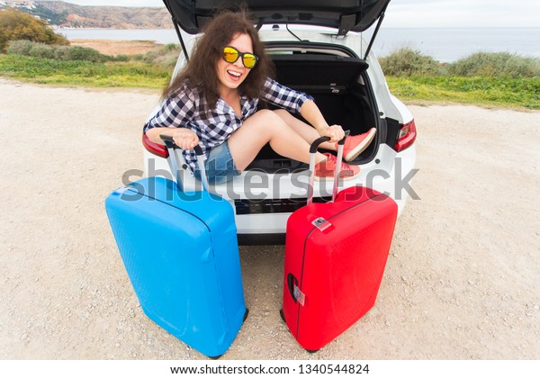 Girl sitting in back of car smiling and getting\
ready to go. Young laughing woman sitting in the open trunk of a\
car. Summer road trip
