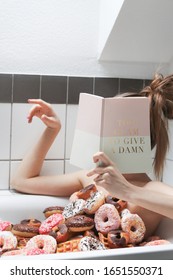 Girl sitting in a bath tub with donuts and reading a glamorous book