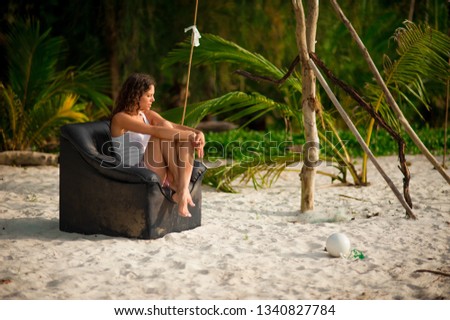 girl sitting in a black leather chair on a sandy beach in Thailand