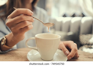 A Girl Is Sitting In A Cafe. Drinking Tea. Coffee. White Cup With Coffee. Stir Sugar. Holds A Cup Of Coffee In His Hand. Pastel Shades. Close-up