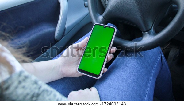 Girl sitting in a\
car and looking at the screen in the phone. Woman holding\
smartphone with empty\
screen.