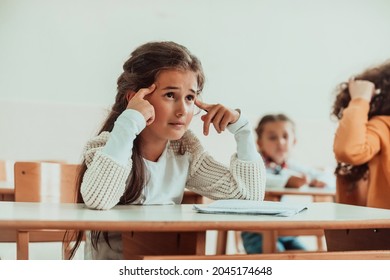 The girl sitting confusedly with her hands on her head in the school desk and attends classes. Selective focus . High quality photo