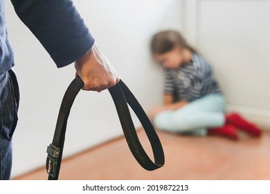 The girl is sitting in the corner hiding from her abusive stepfather. The concept of raising children through domestic violence. Punishment for a crime with a belt. The problem of child abuse.